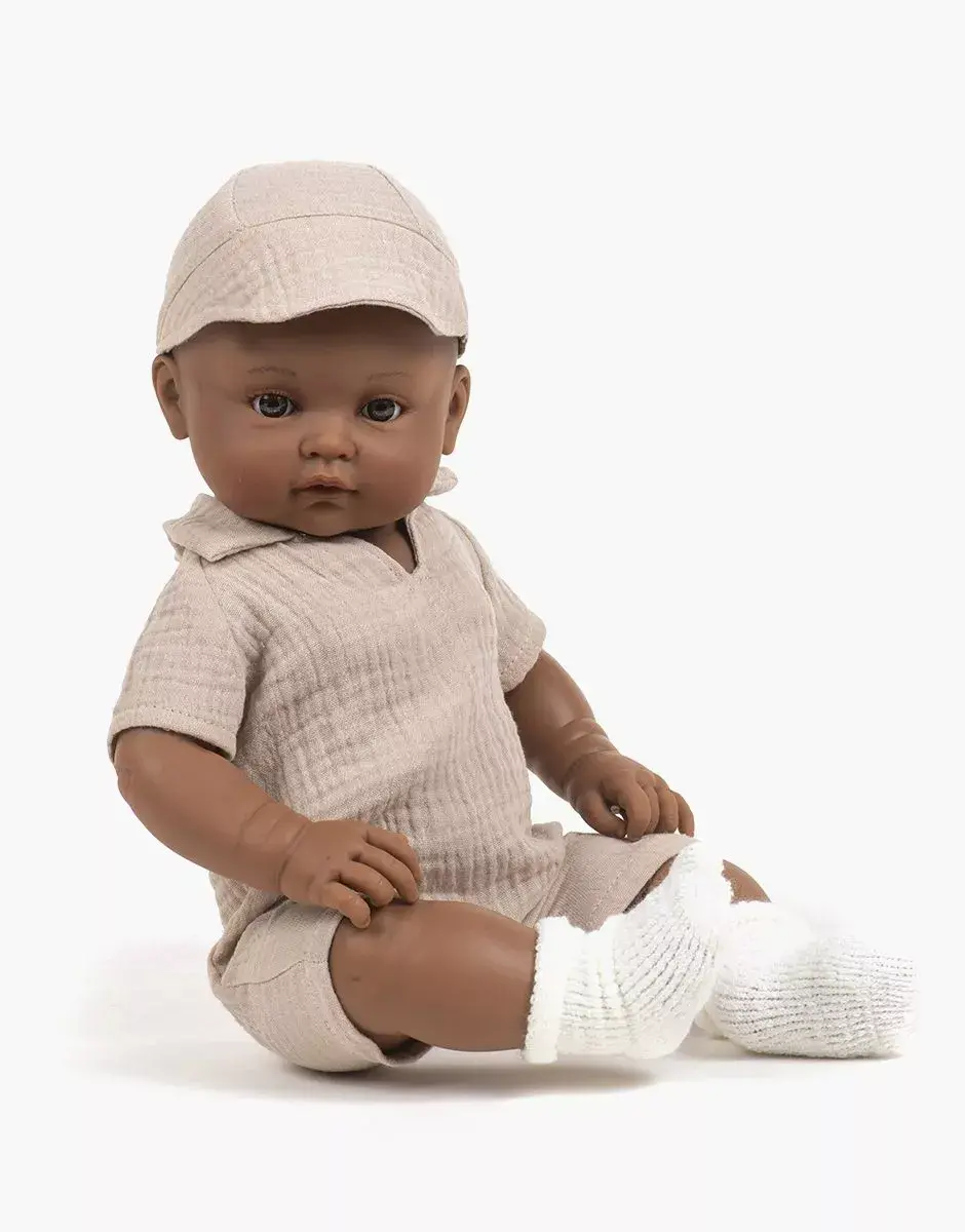 minikane-vetements-poupees-bambinis-47cm-augustin-habille-de-son-ensemble-combinaison-tom-et-casquette-en-double-gaze-beige-assis.webp